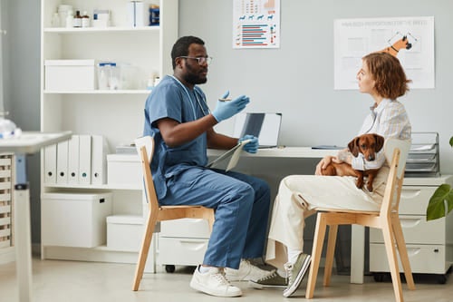 Profissional de saúde explicando informações em um consultório enquanto paciente segura um cachorro