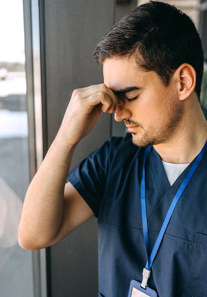 Veterinário em uniforme azul pressionando a testa perto de uma janela