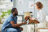 Veterinário examinando um cachorro pequeno com a dona em um consultório
